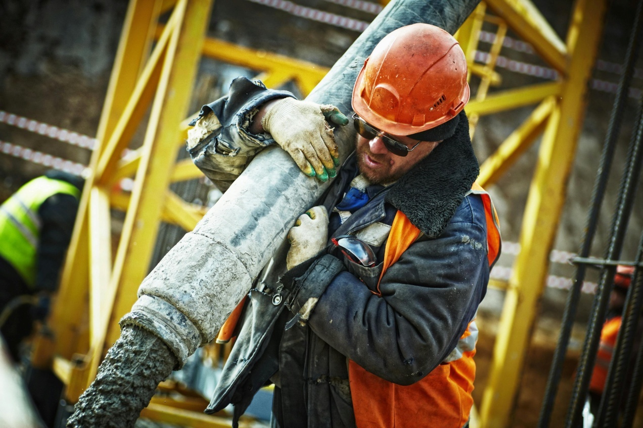 A worker carrying a gray pipe.