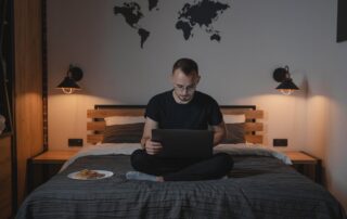 A man using a laptop while sitting on a bed