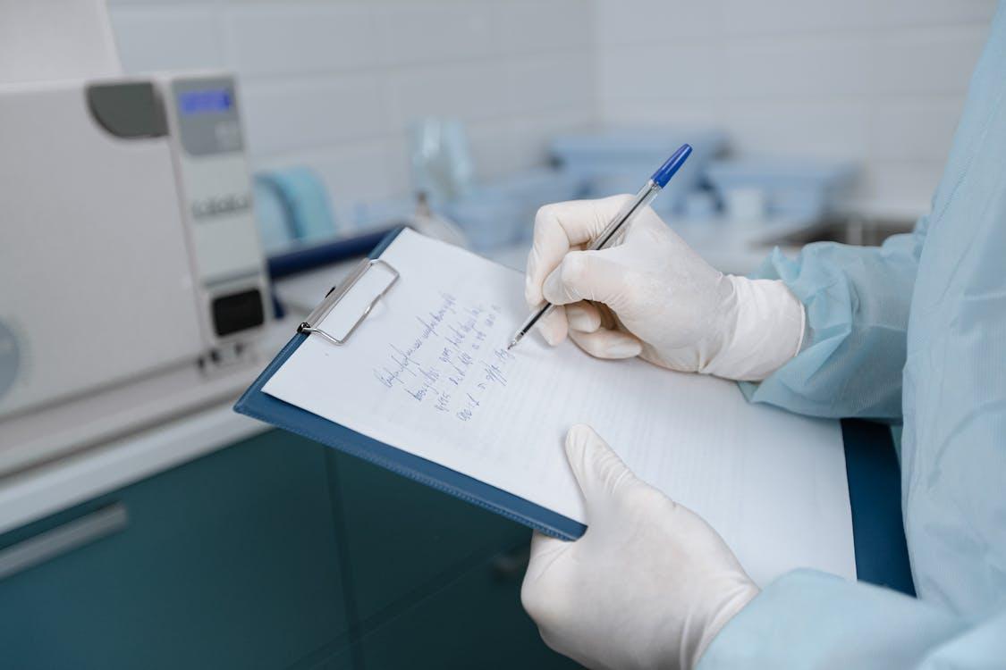 a doctor wearing a medical suit using a clipboard with paper to write notes