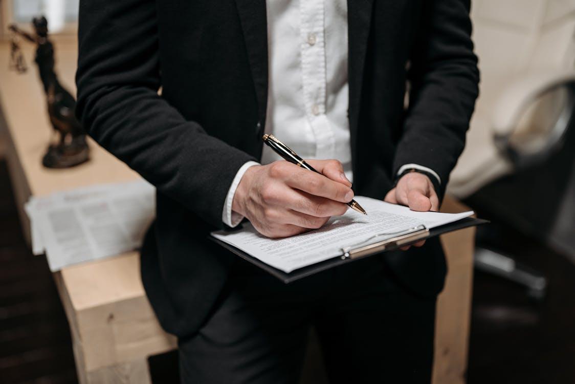 a lawyer in a black suit filing forms on a clipboard with a pen