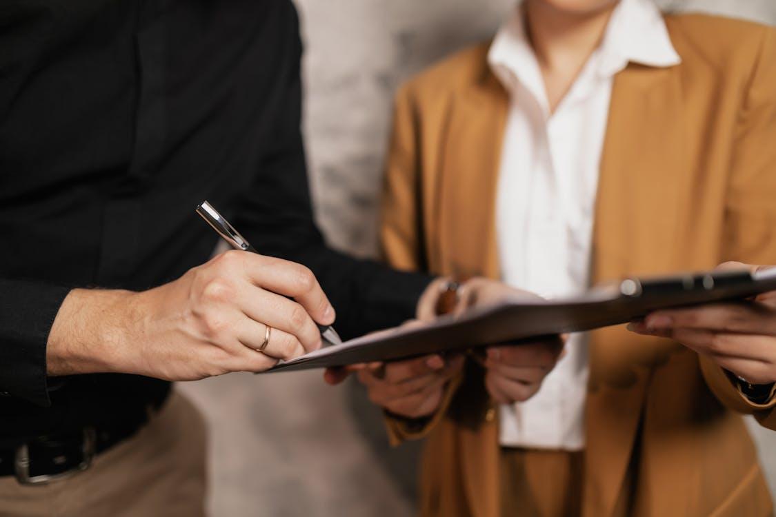 a person holding forms being signed by another person using a pen