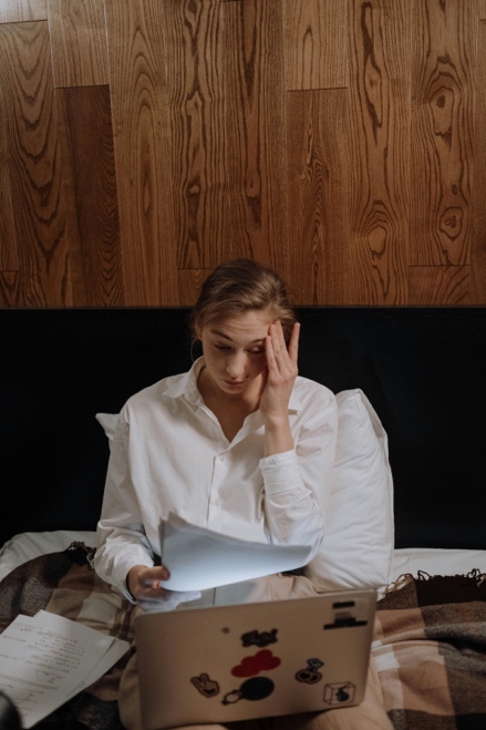 Woman sitting upright in bed, working on a laptop, and appearing stressed