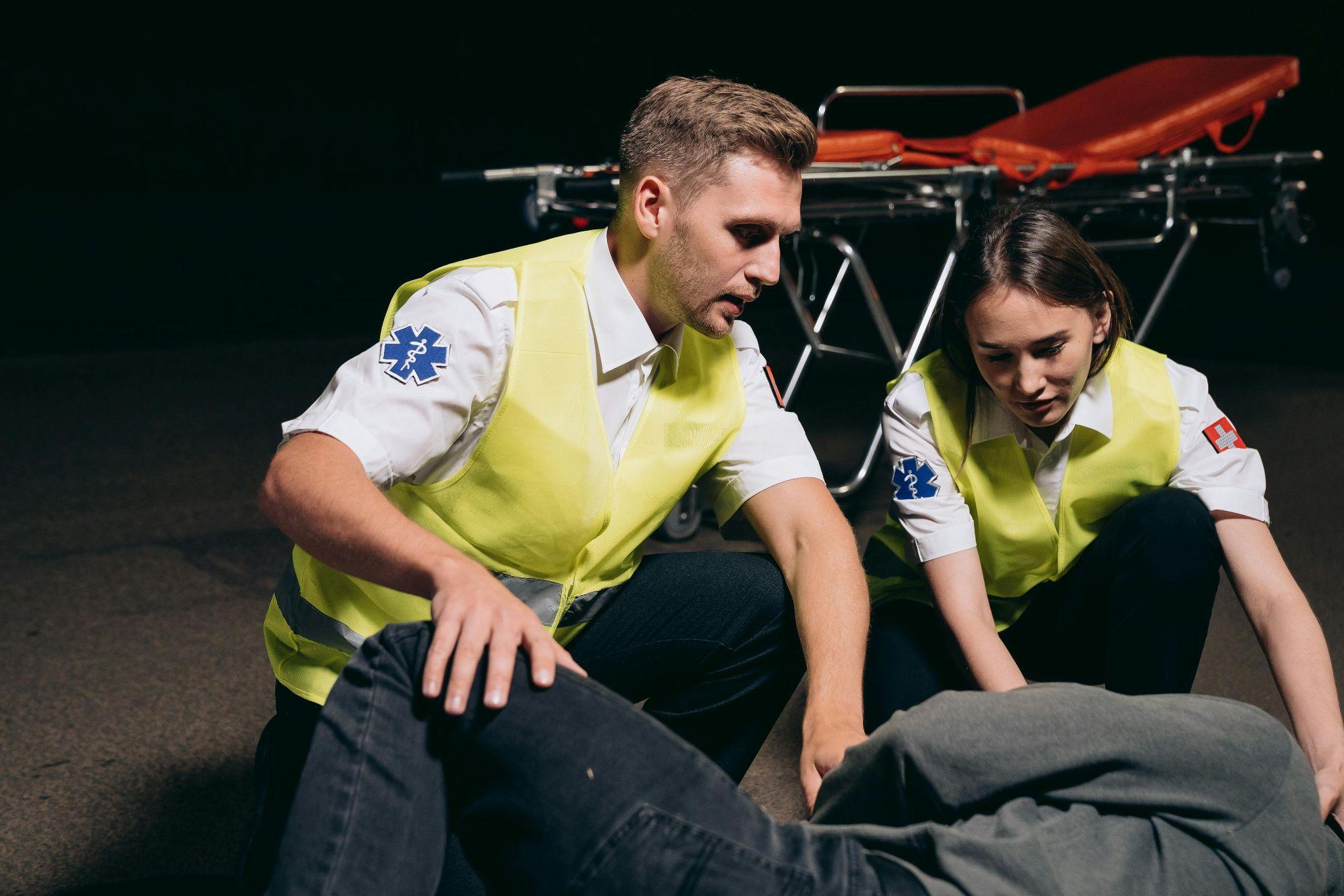 Two paramedics kneeling and helping an injured worker.