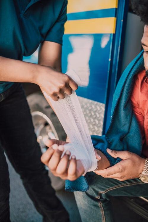 An image of a man wrapping a bandage on another man’s hand